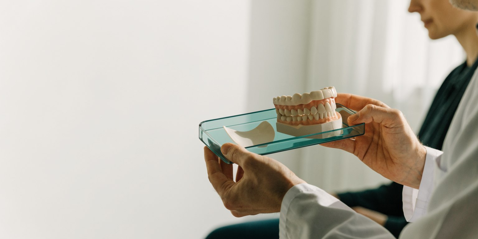 Dentist explaining a ceramic veneer sample and dental model to a patient