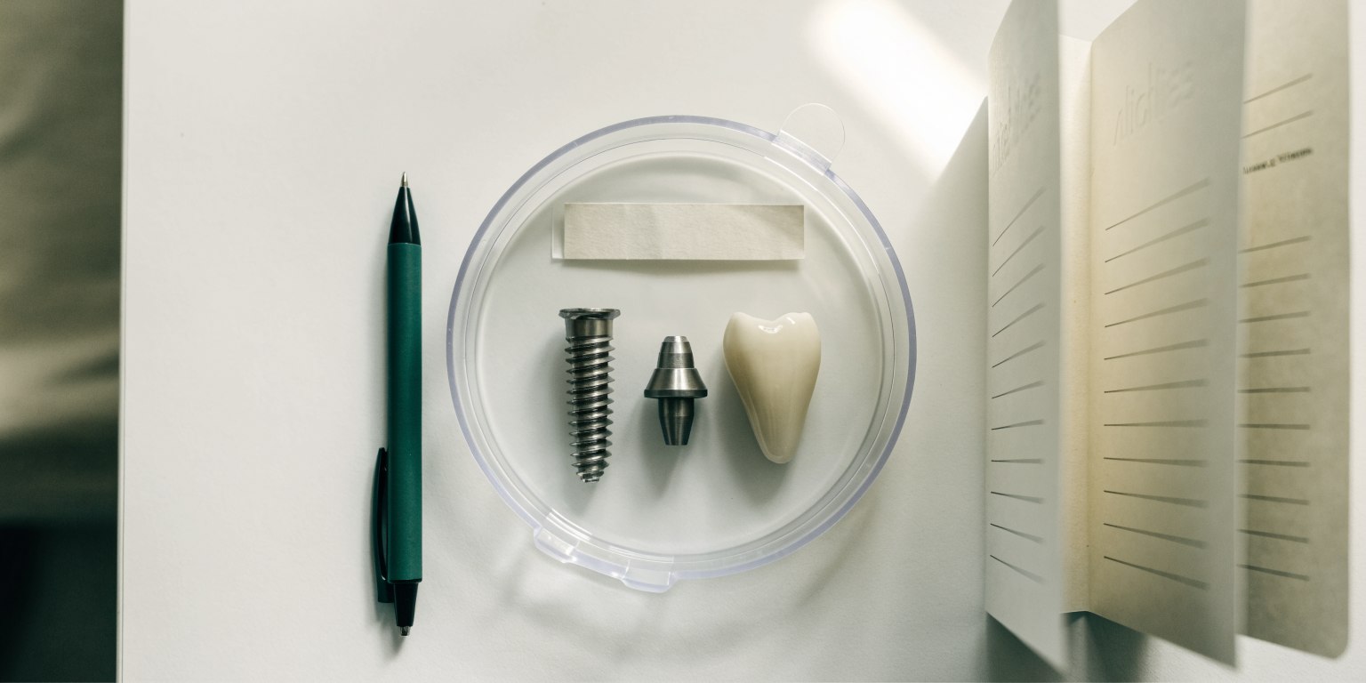 Implant record card beside an implant, abutment and коронка on a clinic desk