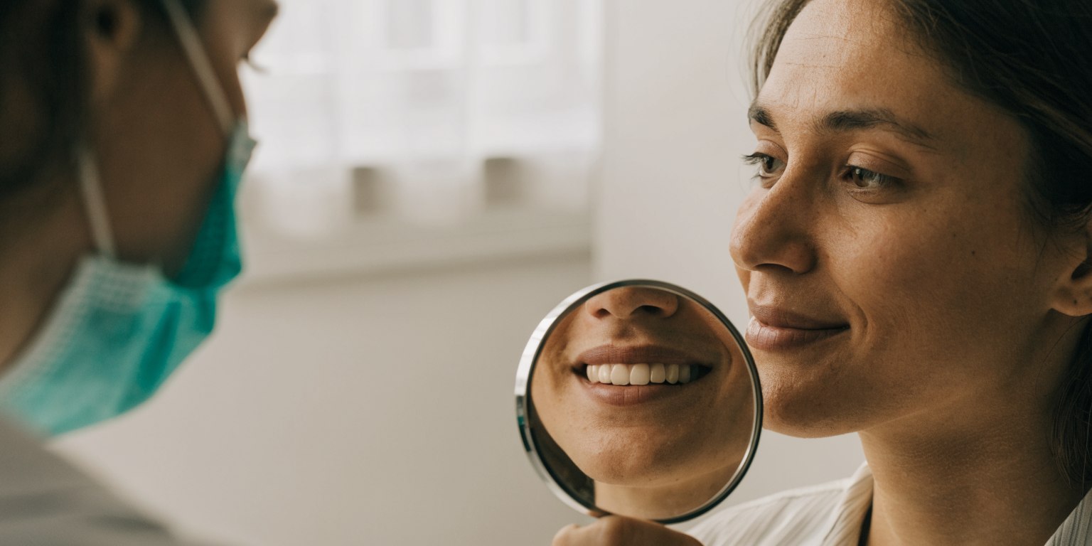 A patient looks at their natural smile in a hand mirror during a dental consultation