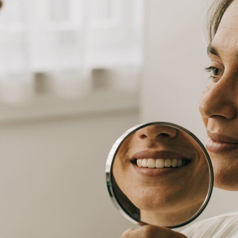 A patient looks at their natural smile in a hand mirror during a dental consultation